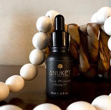 Load image into Gallery viewer, Pure Mimose Diffusing Oil bottle surrounded by white wooden beads with a straw vase in the background