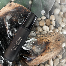 Charger l'image dans la galerie, Pure Sakkara Roll-On fragrance bottle displayed on a light wood log, leaf, and stone background