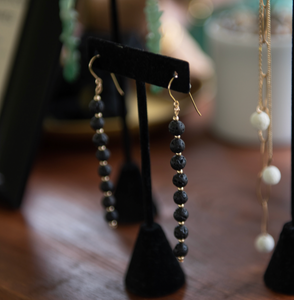 Hatshepsut Fragrance Diffusing Earrings displayed on a black earrings stand white a gold and pearl necklace in the background