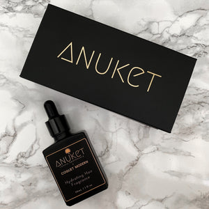 Hydrating hair fragrance bottle and black Anuket box displayed on a white marble background