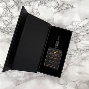 Hydrating hair fragrance bottle inside an opened black box on a white marble background
