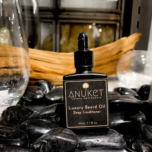 Anuket Luxury Apothecary's Luxury Beard Oil Deep Conditioner for beard growth formula sitting on black stones in front of a a piece of driftwood