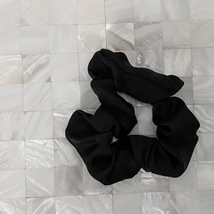 Black satin Scrunchie displayed on a white tile background
