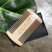 Load image into Gallery viewer, Sandal wood beard comb displayed on its black leather cover on a leaf and wood background
