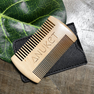Sandal wood beard comb displayed on its black leather cover on a leaf and wood background