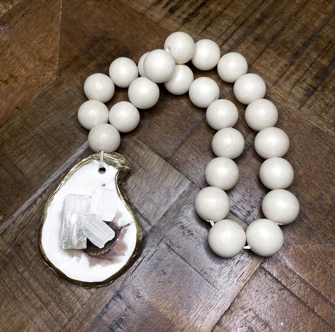 Gold glided oyster attached to white wooden blessing beads loop holding Moroccan selenite crystals on a wooden background