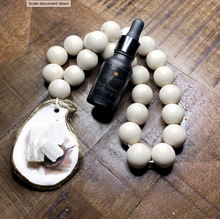 Load image into Gallery viewer, Gold glided oyster attached to a white wooden white blessing beads loop holding white Moroccan selenite crystals white a black Anuket diffusing oil bottle resting on them displayed on a wooden background