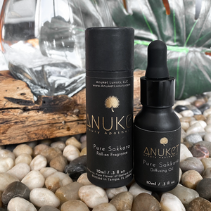 Pure Sakkara diffusing oil bottle and Pure Sakkara roll on fragrance displayed on a background of leaves, stones and a log of wood
