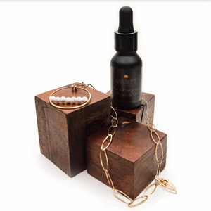 Fragrance Diffusing Demi-Fine Jewelry laying on 3 wooden blocks with a pure papyrus diffusing oil bottle on a white background