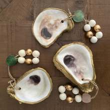 Load image into Gallery viewer, Three gold glided oyster dishes attached to white and gold wooden blessing beads small loops two of them with a green stone and one with a light pink stone on a wooden background