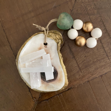 Load image into Gallery viewer, Gold glided oyster dish attached to a gold and white wooden blessing beads with a green stone small loop on a wooden background