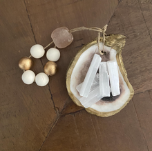 Load image into Gallery viewer, Gold glided oyster dish holding white Moroccan selenite stick attached to a white and gold wooden blessing bead loop and a light pink stone loop displayed on a wooden background