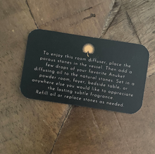 Load image into Gallery viewer, Small black card with Anuket gold logo with product info writing on a wooden background