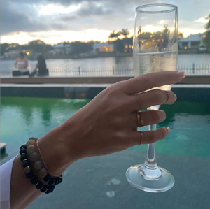 Hand holding a glass of champagne wearing THE ANUKET Fragrance Diffusing Bracelet
