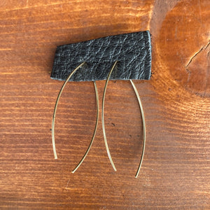 Gold marquise earrings attached to a black leather piece displayed on a wooden background