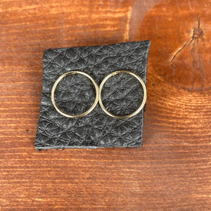 Gold open circle stud earring displayed on black leather piece on a wooden background